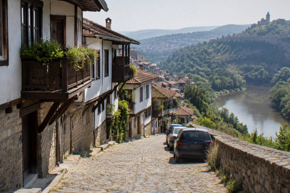 A narrow street in Veliko Tarnovo's old town with parked cars along a stone retaining wall