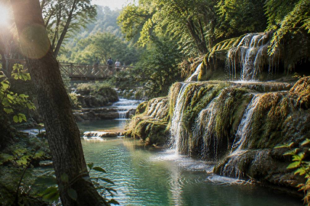 A waterfall spilling over travertine ledges into a green pool in a forest