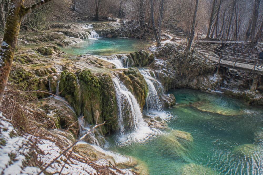 Turquoise water spilling over travertine ledges at a forested Bulgarian waterfall