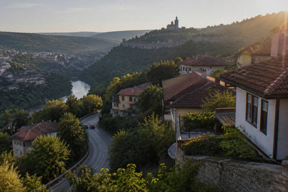 A two-lane road winding through forested Balkan foothills on a clear day