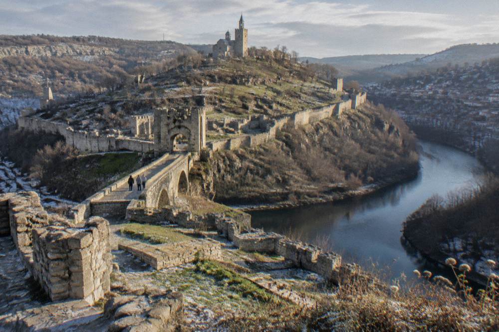 Hillside houses and a fortress wall under an overcast winter sky above a river bend