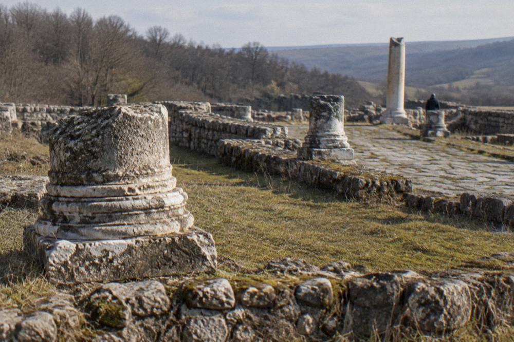 Overgrown stone ruins and column bases of the Roman site Nicopolis ad Istrum in open countryside
