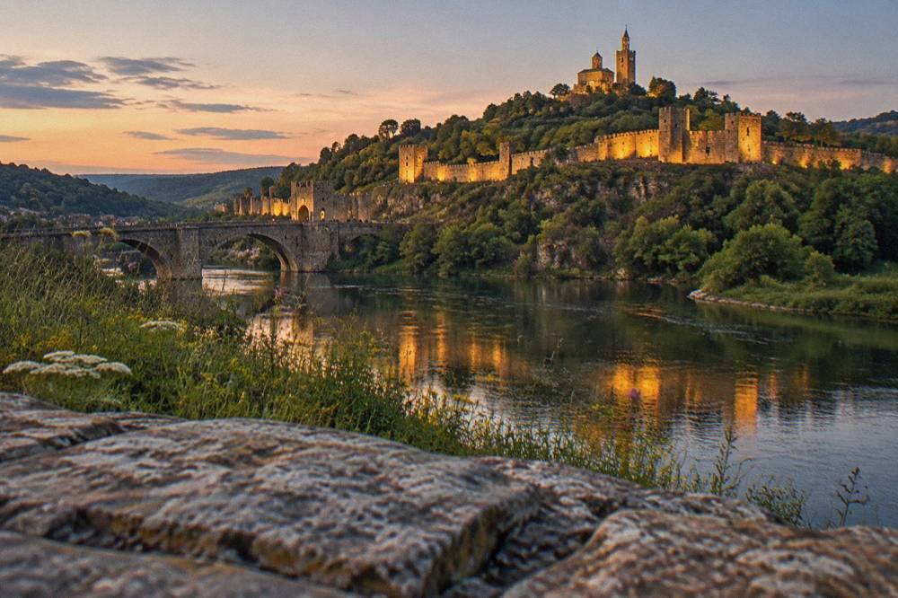 Illuminated walls and towers of Tsarevets Fortress seen across the Yantra river at dusk