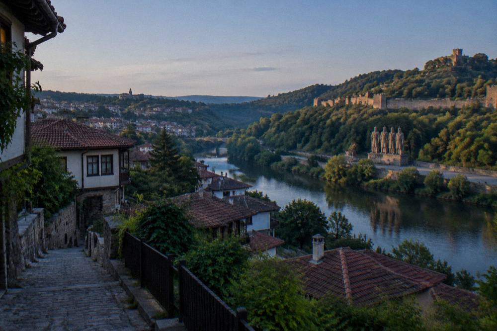 A stone monument of four medieval kings standing beside the river opposite a fortress hill