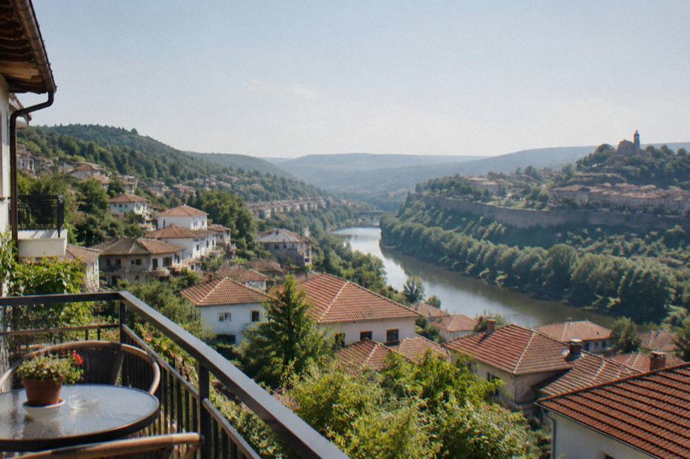 A hotel balcony above red rooftops with the river valley and hills beyond