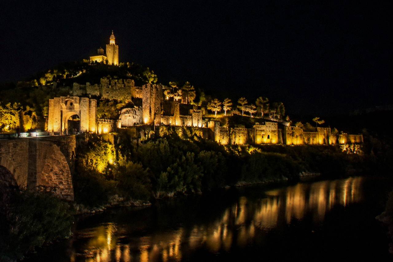 Illuminated fortress walls on a hill above a dark river at night