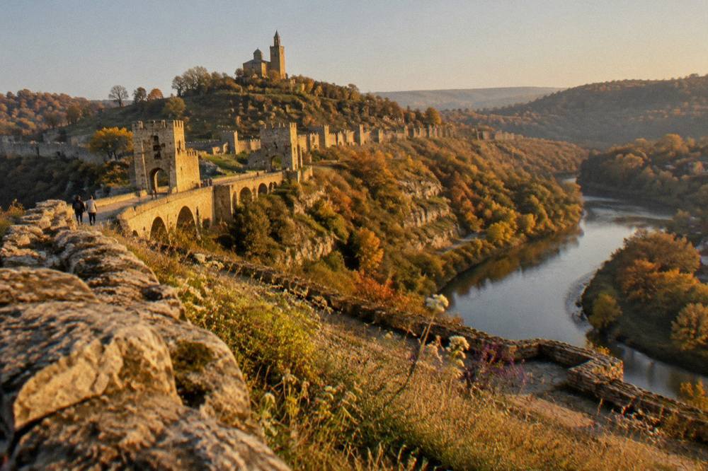 A hilltop fortress wall above a river bend with autumn trees below