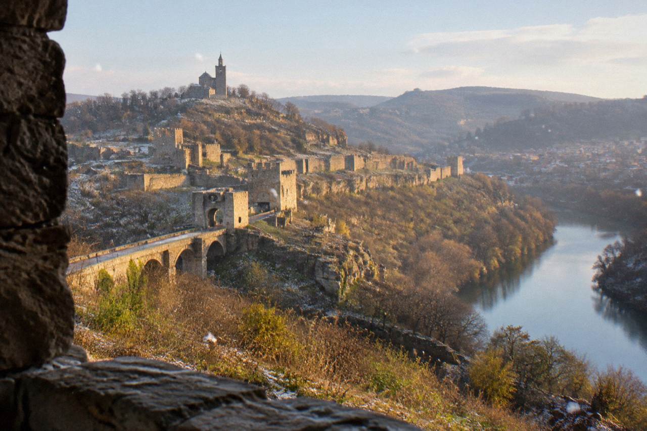 Medieval fortress walls on a hill above a river bend in a Bulgarian city at dusk