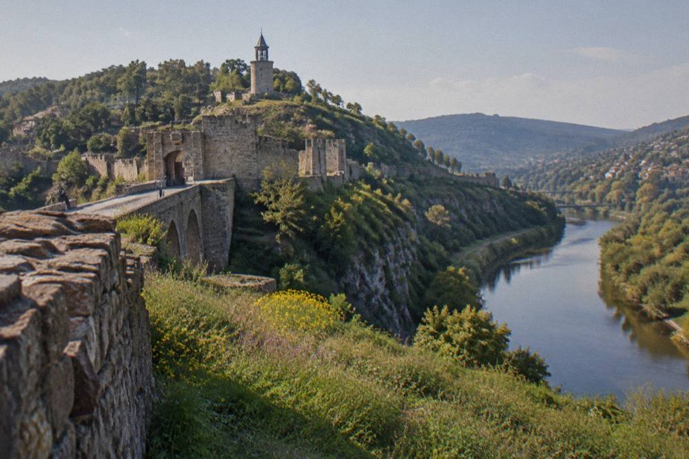 Stone fortress walls and a round tower on a hilltop above a river