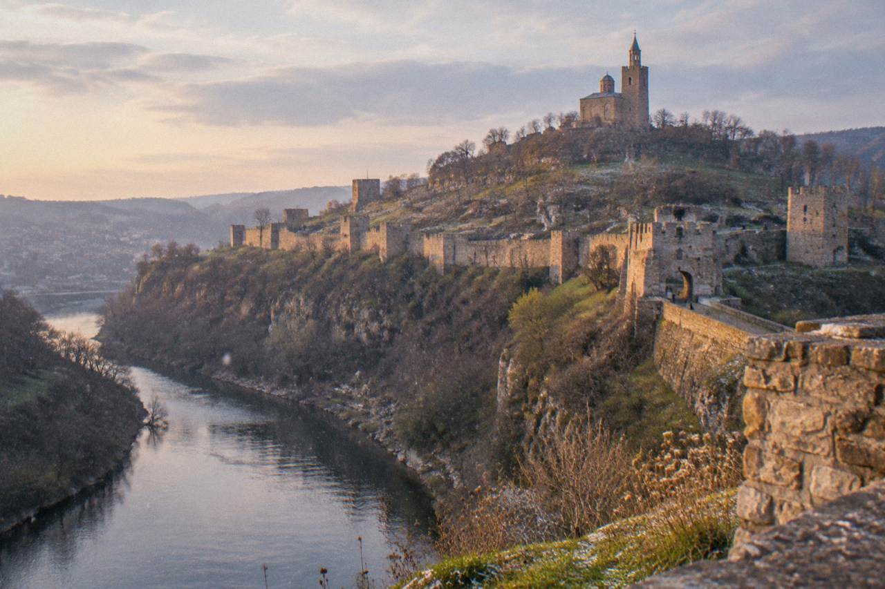 The stone walls and towers of Tsarevets Fortress rising above the Yantra river at dusk