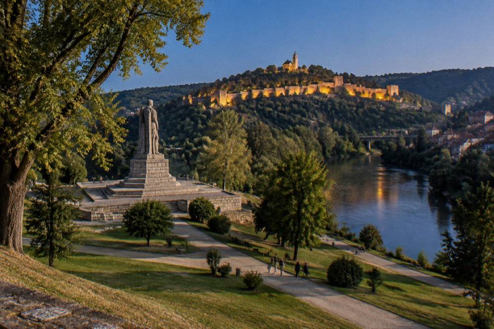 The Asenevtsi Monument beside the Yantra river with the illuminated fortress hill behind it at night