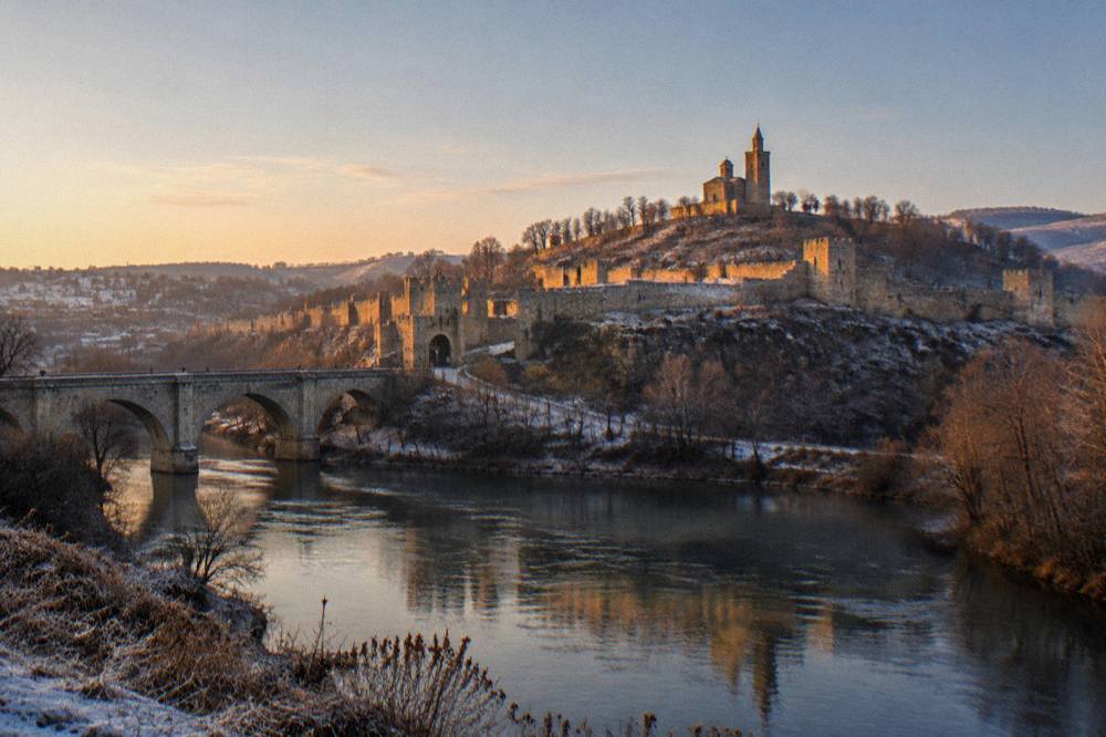 The illuminated Tsarevets Fortress hill seen at dusk from across the Yantra river