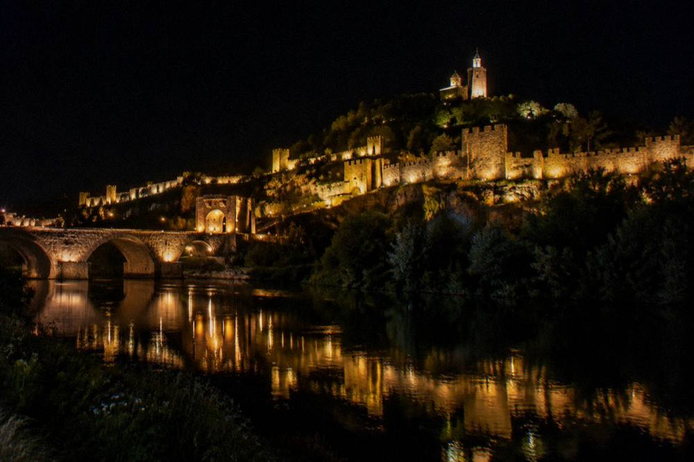 The illuminated walls of Tsarevets fortress reflected in the Yantra river at night